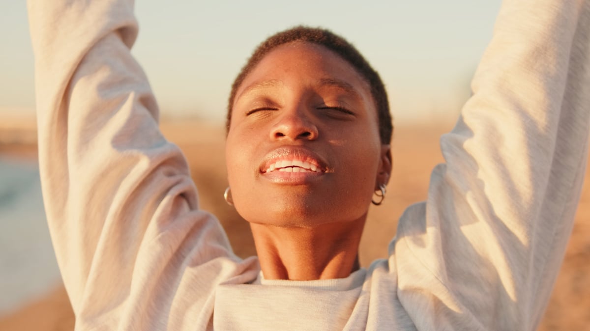 A girl smiles and raises her arms to the sky at dawn on the beach