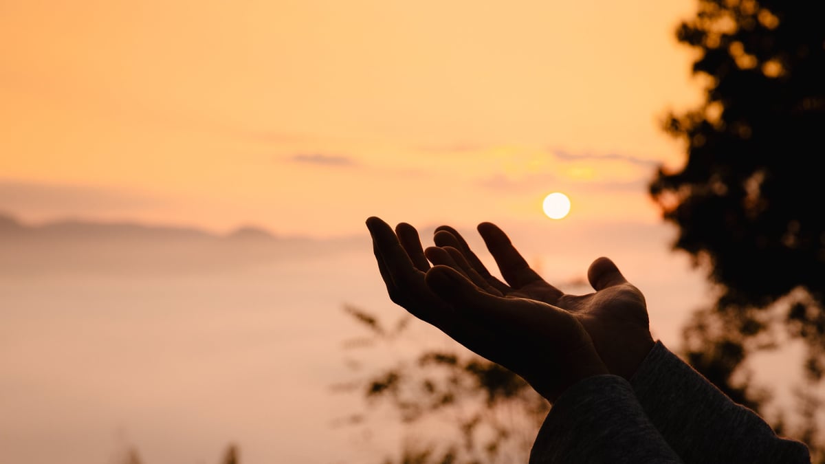 Woman in silhouette, worship in prayer at sunrise with sun rising in summer sky, embracing her faith amidst beauty of nature.
