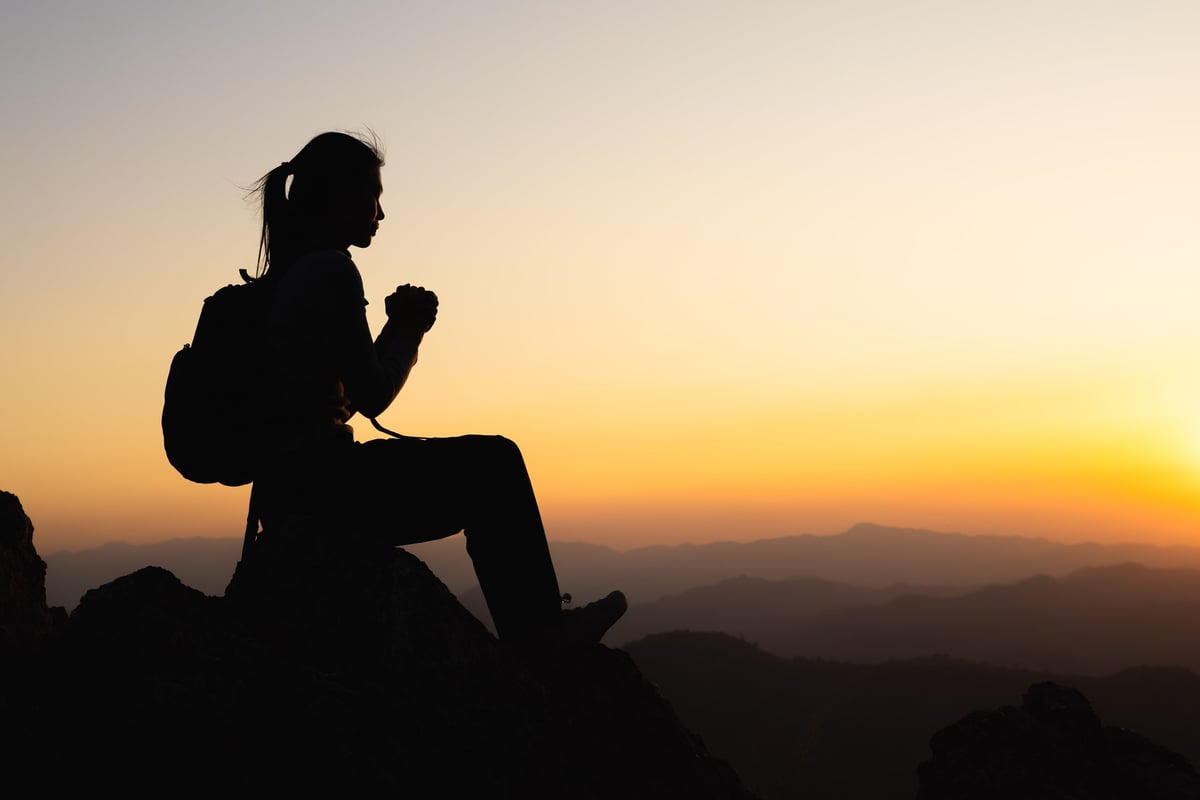 Silhouette of a women is praying to God on the mountain. Praying hands with faith in religion and belief in God on blessing background. Power of hope or love and devotion.